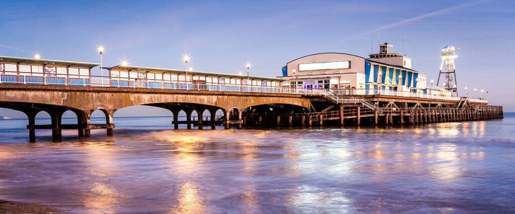 Bournemouth Pier at night Dorset. The lights of Bournemouth Pier at night reflected in the wet sand on the beach. Dorset England UK Europe.